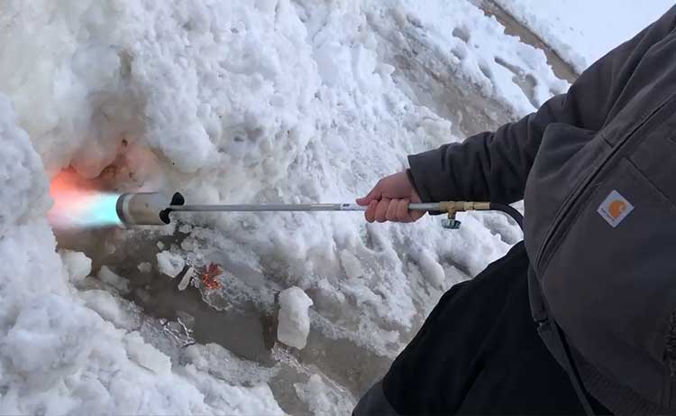 Handheld gas torch melting ice and snow at a poultry facility.